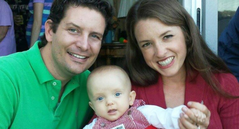mother and father hold newborn while smiling